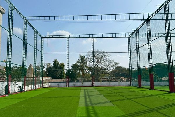 Outdoor practice cage with tall metal frame and netting, surrounding a green artificial turf field under a blue sky.