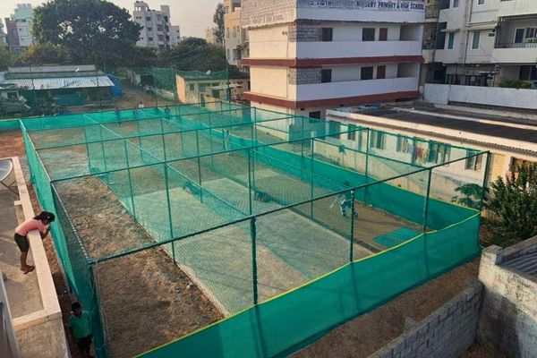 Green netted cricket/athletics practice nets on a rooftop, with surrounding buildings visible in the background.